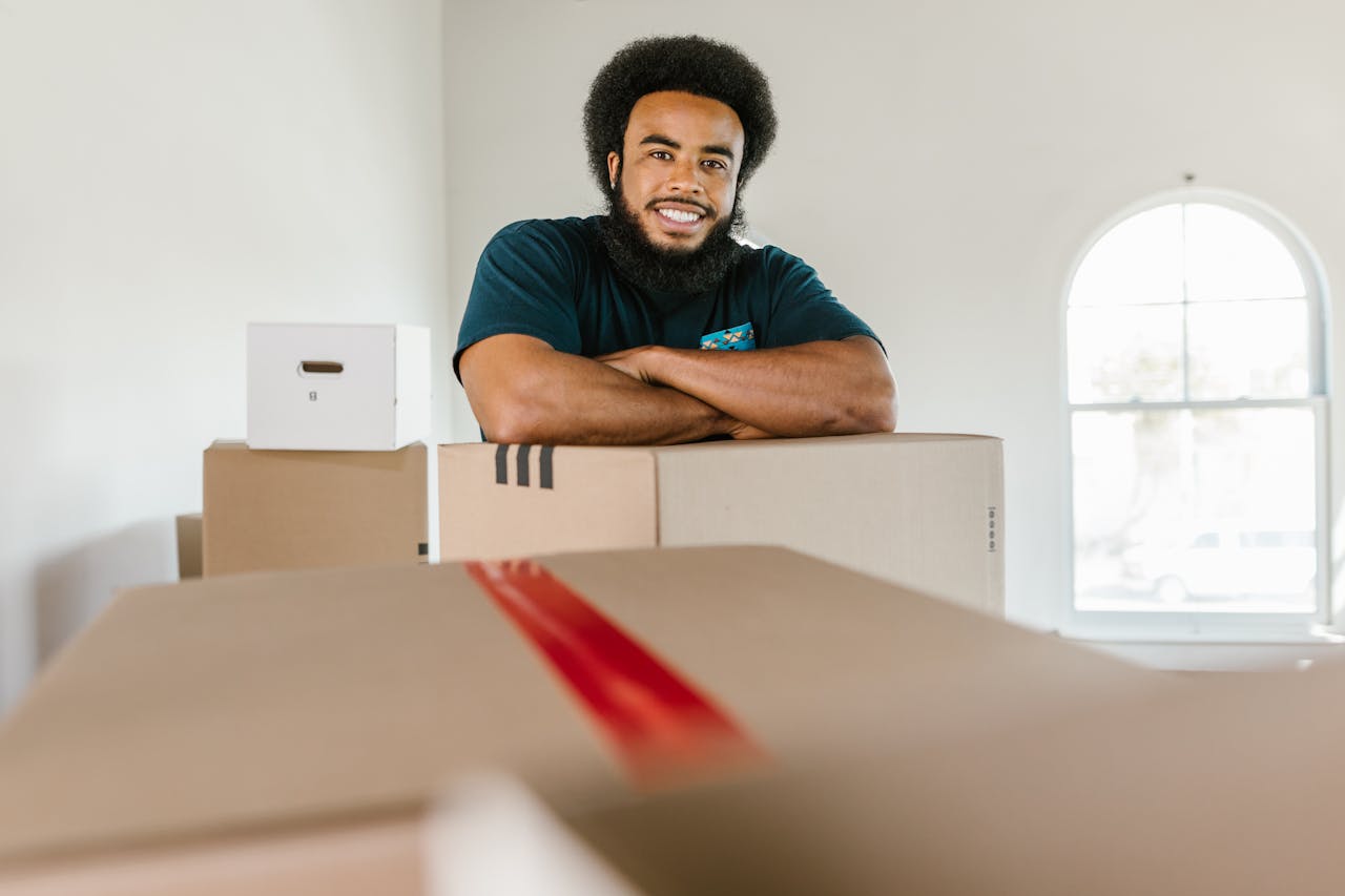 A cheerful mover standing with packed boxes indoors, ready for a moving day.